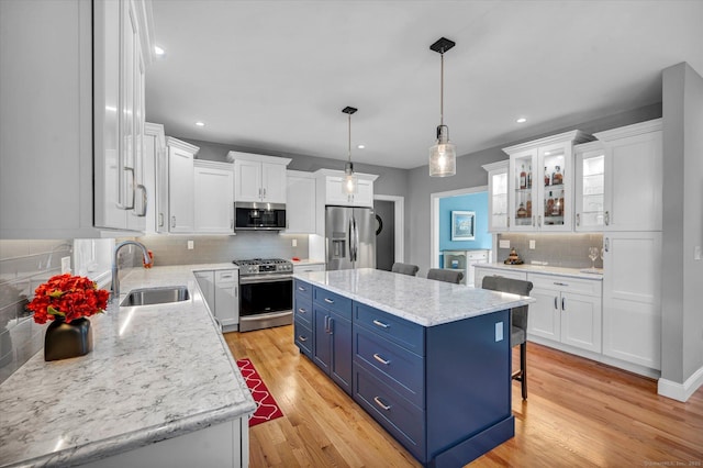 kitchen with appliances with stainless steel finishes, blue cabinetry, a kitchen island, white cabinetry, and decorative light fixtures