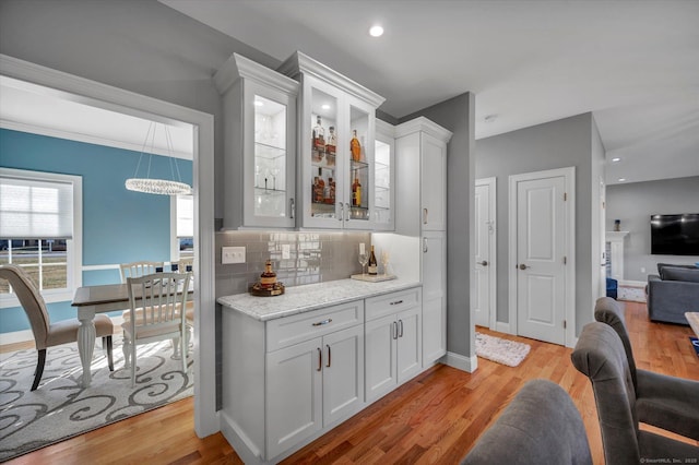 bar with a chandelier, light wood-type flooring, light stone counters, white cabinetry, and backsplash