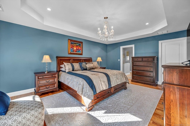 bedroom with a raised ceiling, light hardwood / wood-style floors, and a chandelier