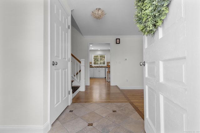 entryway with light wood-style floors, crown molding, stairs, and baseboards