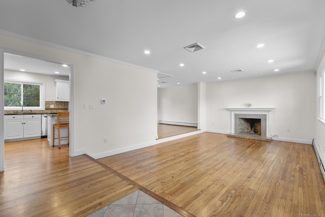 unfurnished living room with visible vents, a fireplace with raised hearth, light wood-style floors, crown molding, and baseboards