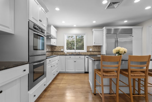 kitchen featuring stainless steel appliances, a kitchen bar, visible vents, and white cabinetry