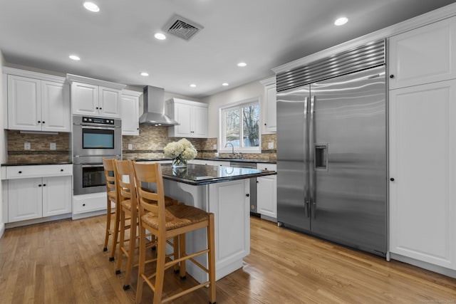 kitchen with light wood finished floors, visible vents, appliances with stainless steel finishes, and wall chimney range hood