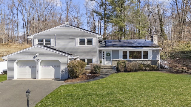 split level home with a front lawn, aphalt driveway, roof mounted solar panels, an attached garage, and a chimney