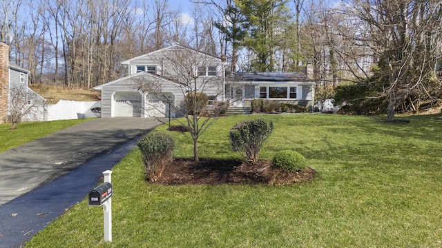 split level home with solar panels, fence, aphalt driveway, a front yard, and an attached garage