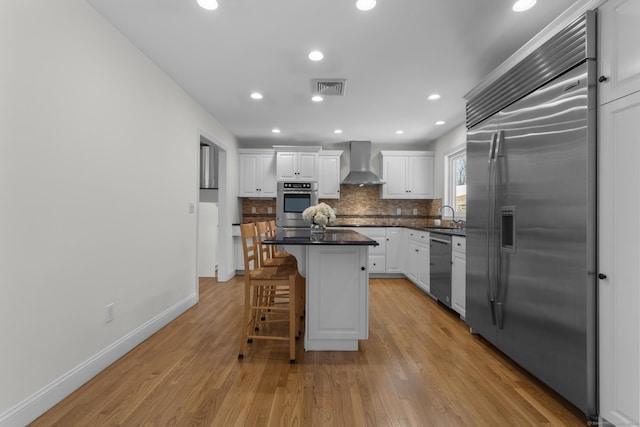 kitchen with visible vents, dark countertops, white cabinetry, appliances with stainless steel finishes, and wall chimney range hood