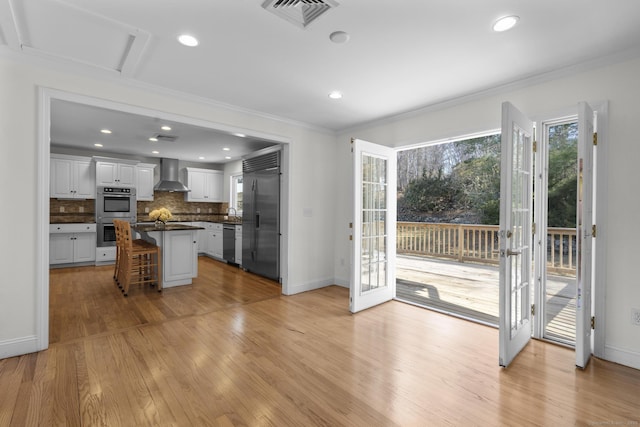 kitchen featuring visible vents, stainless steel appliances, a kitchen bar, dark countertops, and wall chimney range hood