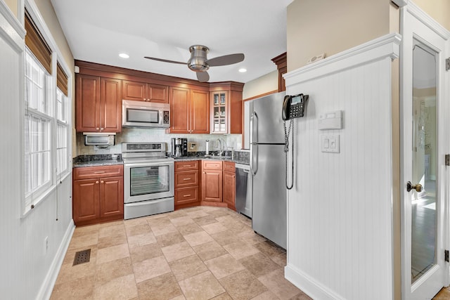 kitchen featuring stainless steel appliances, tasteful backsplash, dark stone countertops, sink, and ceiling fan