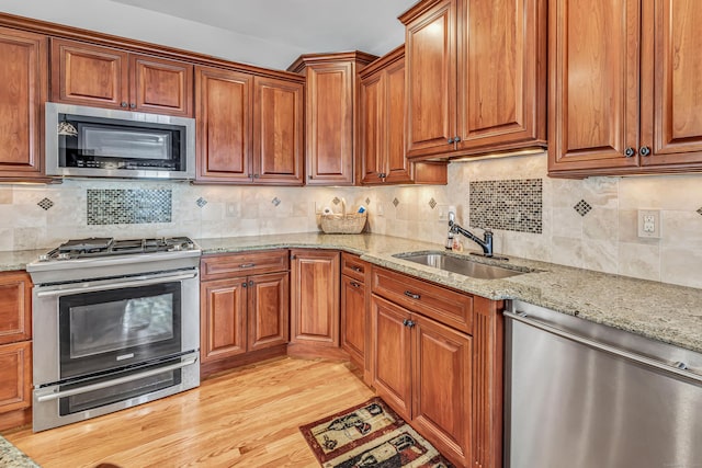 kitchen with appliances with stainless steel finishes, backsplash, light stone counters, and sink