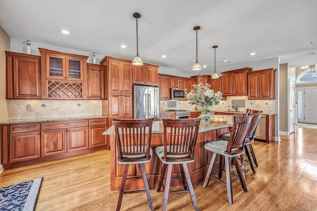 kitchen featuring a center island, light hardwood / wood-style flooring, decorative light fixtures, light stone counters, and stainless steel appliances