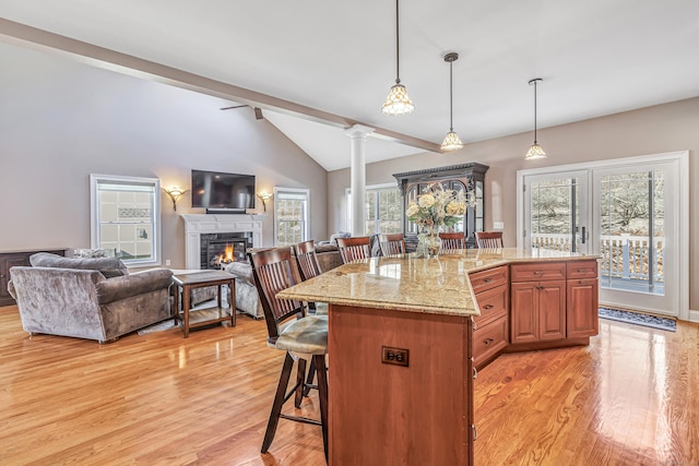 kitchen with light stone counters, decorative columns, decorative light fixtures, a breakfast bar, and a kitchen island