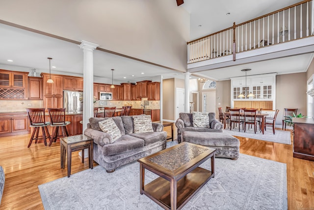 living room featuring a towering ceiling, light wood-type flooring, and ornate columns