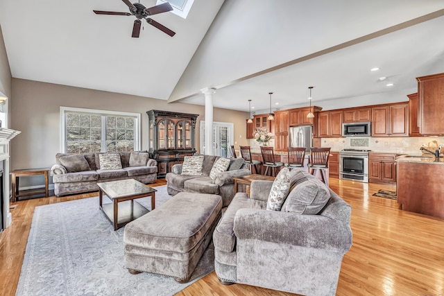 living room featuring ornate columns, ceiling fan, sink, high vaulted ceiling, and light wood-type flooring