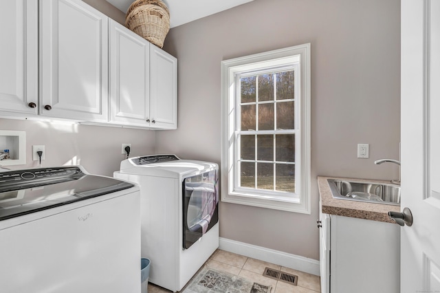 clothes washing area with cabinets, washing machine and dryer, a wealth of natural light, and sink