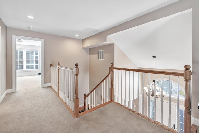 hall with light colored carpet and an inviting chandelier