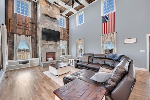 living room featuring coffered ceiling, light hardwood / wood-style flooring, a towering ceiling, a fireplace, and beamed ceiling