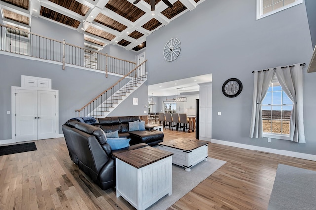 living room featuring a high ceiling, coffered ceiling, light wood-type flooring, beamed ceiling, and a chandelier