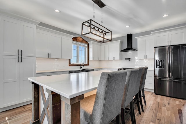 kitchen with a center island, white cabinets, wall chimney exhaust hood, stainless steel fridge, and decorative light fixtures