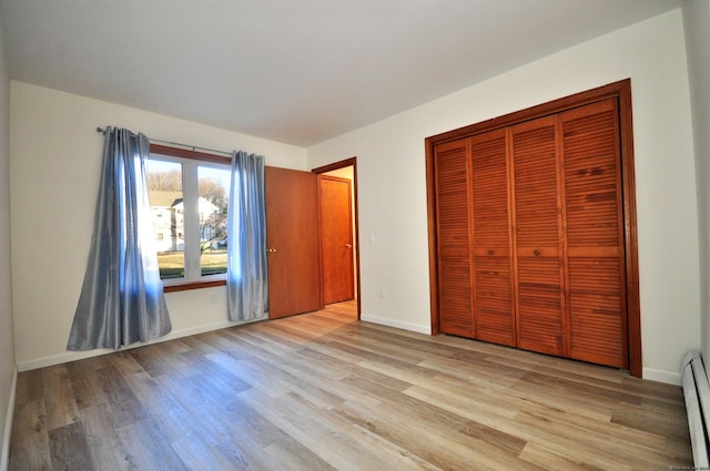 unfurnished bedroom featuring light hardwood / wood-style floors, baseboard heating, and a closet