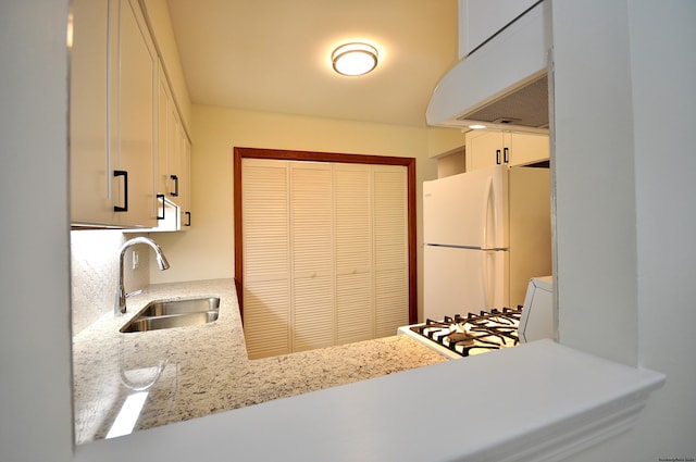 kitchen with white fridge, white cabinets, light stone countertops, and sink