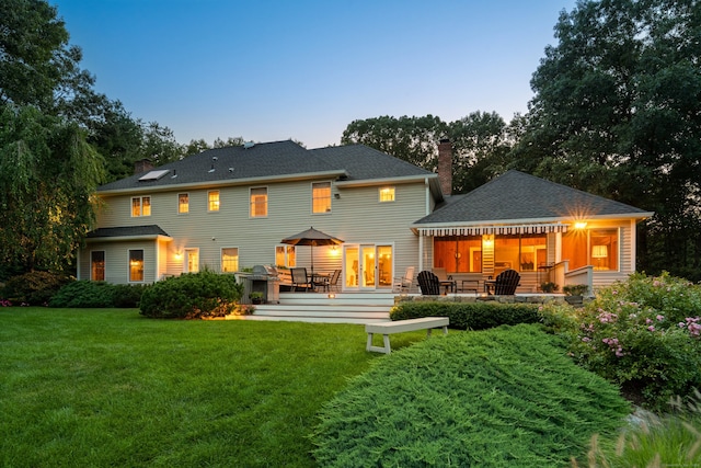 back house at dusk featuring a lawn and a patio