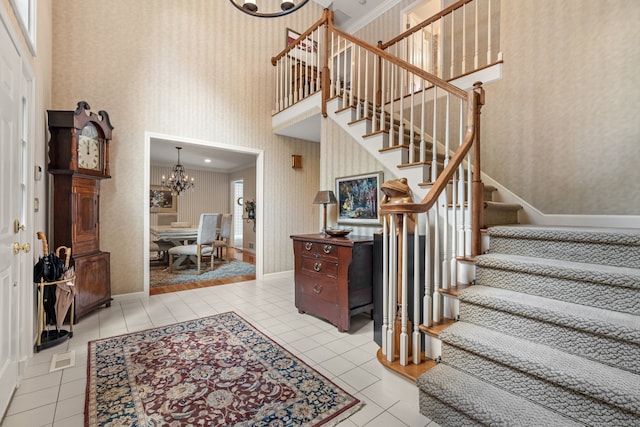 tiled foyer with crown molding, a chandelier, and a high ceiling