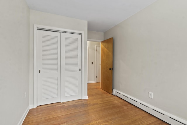 unfurnished bedroom featuring a closet, light hardwood / wood-style flooring, and a baseboard heating unit