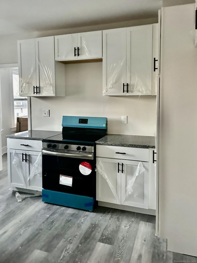 kitchen with stainless steel range, light wood-type flooring, white cabinetry, and dark stone countertops