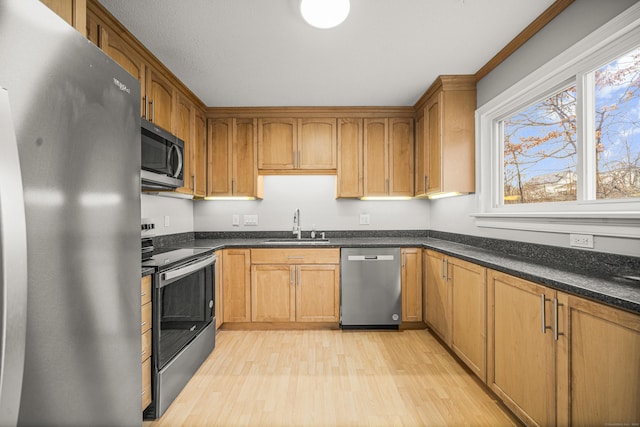 kitchen featuring stainless steel appliances, light hardwood / wood-style flooring, dark stone counters, and sink