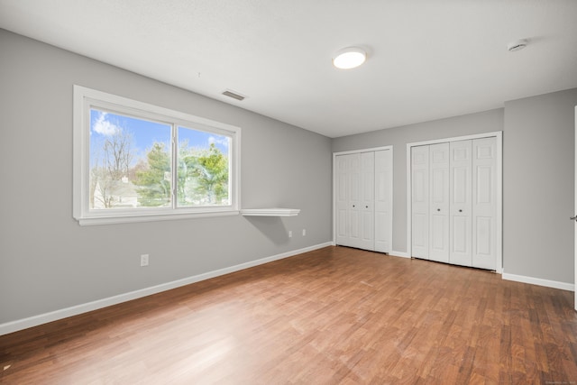 unfurnished bedroom with wood-type flooring and two closets