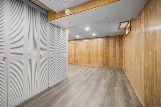 basement featuring light hardwood / wood-style flooring, a drop ceiling, and wood walls