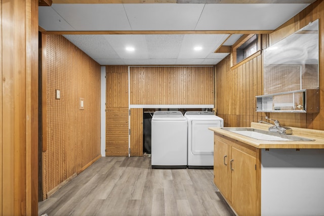 clothes washing area featuring separate washer and dryer, wooden walls, sink, and light wood-type flooring