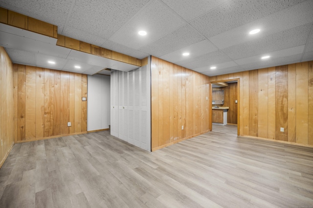 basement with a paneled ceiling, wooden walls, and light hardwood / wood-style flooring