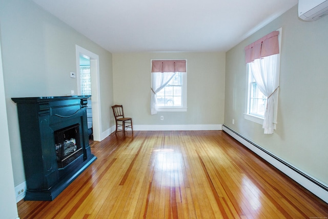 living room with a wall unit AC, a wealth of natural light, light hardwood / wood-style floors, and a baseboard heating unit