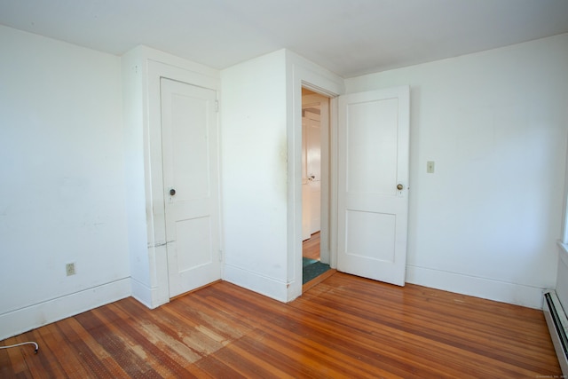 unfurnished bedroom with wood-type flooring, a closet, and a baseboard heating unit