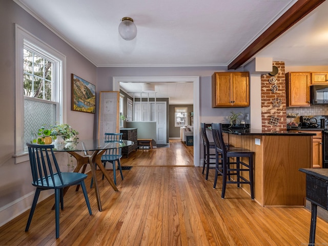 kitchen with a kitchen breakfast bar, backsplash, light wood-type flooring, black appliances, and ornamental molding