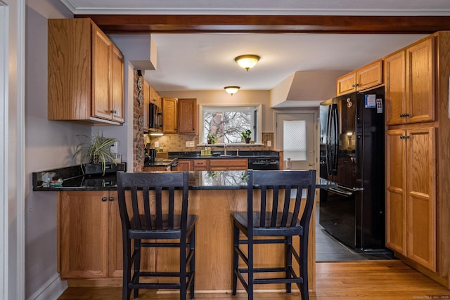 kitchen with sink, tasteful backsplash, wood-type flooring, a kitchen bar, and black appliances