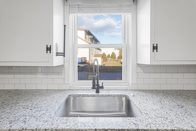 room details featuring white cabinets, backsplash, light stone counters, and sink