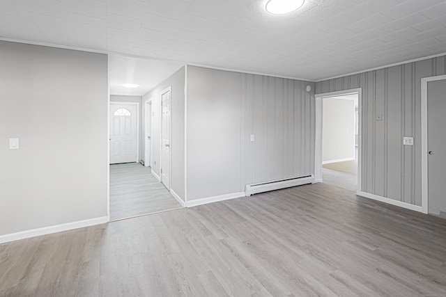 empty room featuring ornamental molding, light wood-type flooring, and a baseboard heating unit