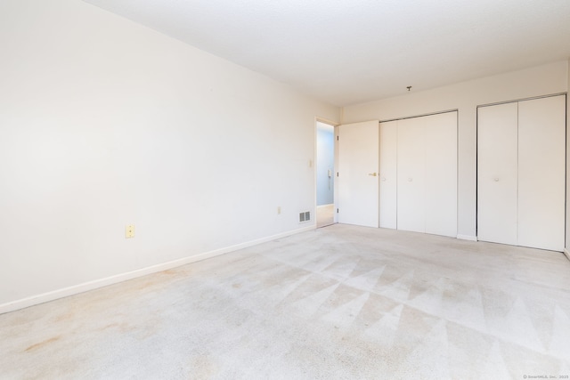 unfurnished bedroom with light colored carpet and two closets