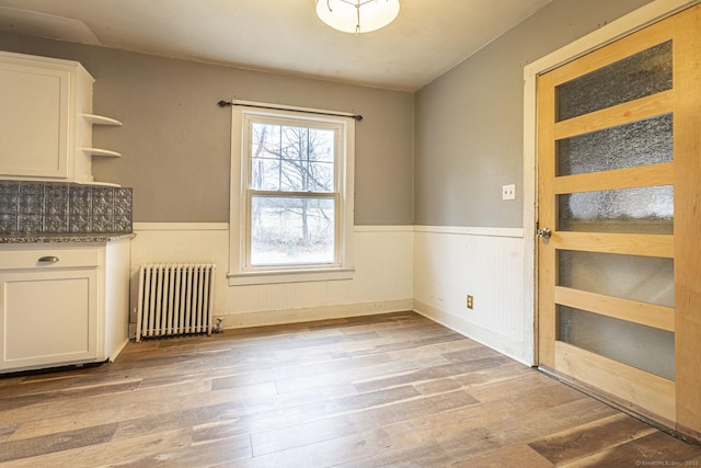 unfurnished dining area featuring radiator heating unit and light hardwood / wood-style flooring