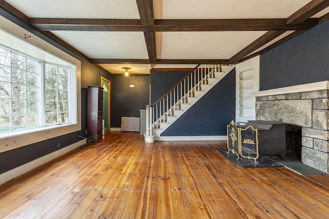 unfurnished living room with coffered ceiling, hardwood / wood-style floors, beamed ceiling, radiator heating unit, and a wood stove