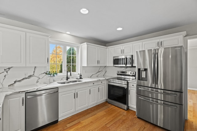 kitchen with white cabinets, sink, light stone countertops, appliances with stainless steel finishes, and light hardwood / wood-style floors