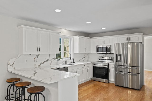 kitchen featuring decorative backsplash, appliances with stainless steel finishes, a kitchen bar, sink, and white cabinetry