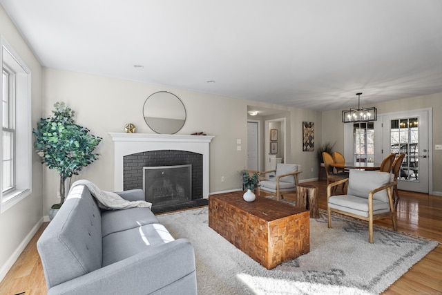 living room featuring plenty of natural light, light hardwood / wood-style floors, a notable chandelier, and a brick fireplace