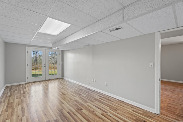 spare room featuring french doors, light wood-type flooring, and a drop ceiling