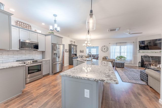 kitchen featuring appliances with stainless steel finishes, backsplash, gray cabinetry, decorative light fixtures, and an island with sink