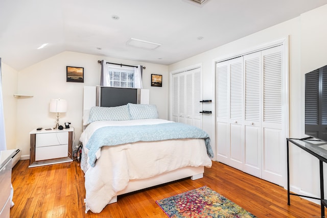 bedroom with lofted ceiling, wood-type flooring, a baseboard radiator, and two closets