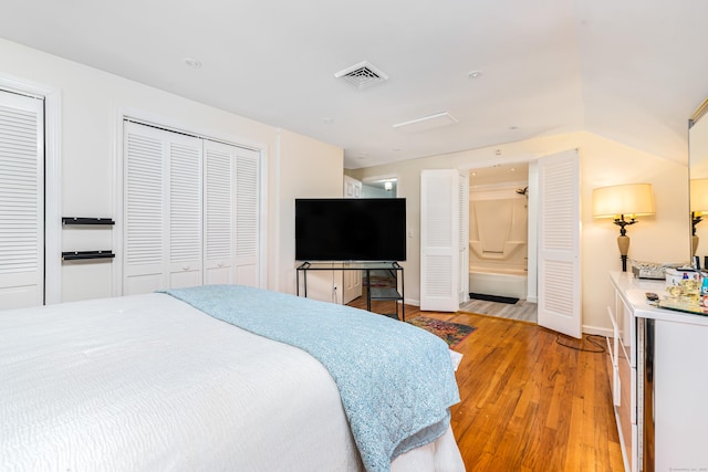 bedroom featuring two closets, ensuite bathroom, and light hardwood / wood-style flooring