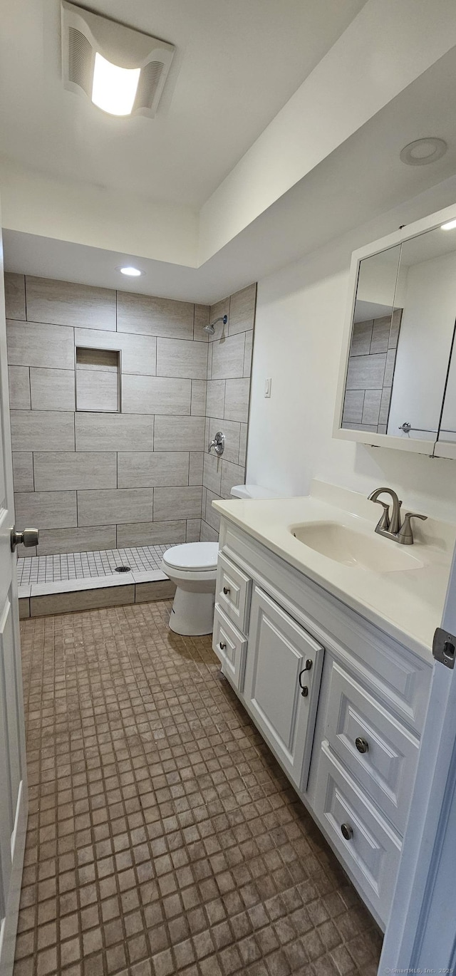 bathroom with toilet, vanity, and a tile shower